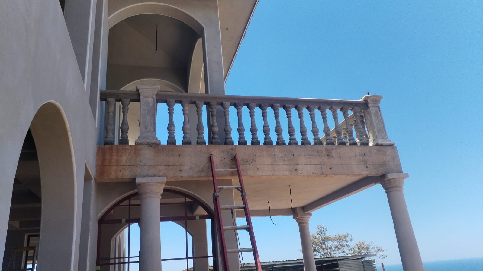 Se observa una estructura de balcón en construcción con barandales de concreto y una escalera apoyada en la fachada.