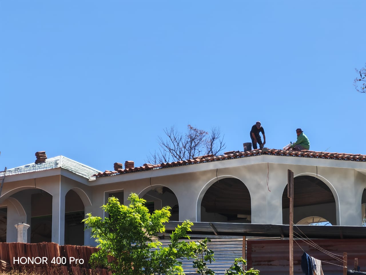 Dos trabajadores realizan labores de mantenimiento o reparación sobre el techo de una casa con arcos.