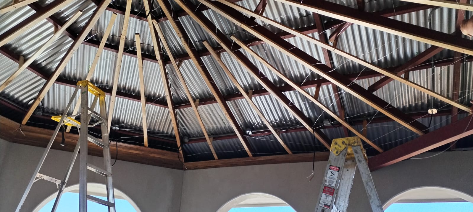 Se observa la estructura de madera y metal de un techo en construcción con escaleras de mano debajo.