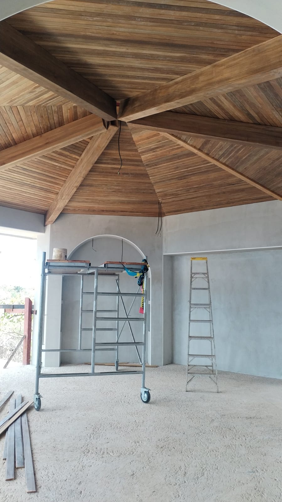 Se observa un espacio interior en construcción con un techo de madera detallado y andamios metálicos.