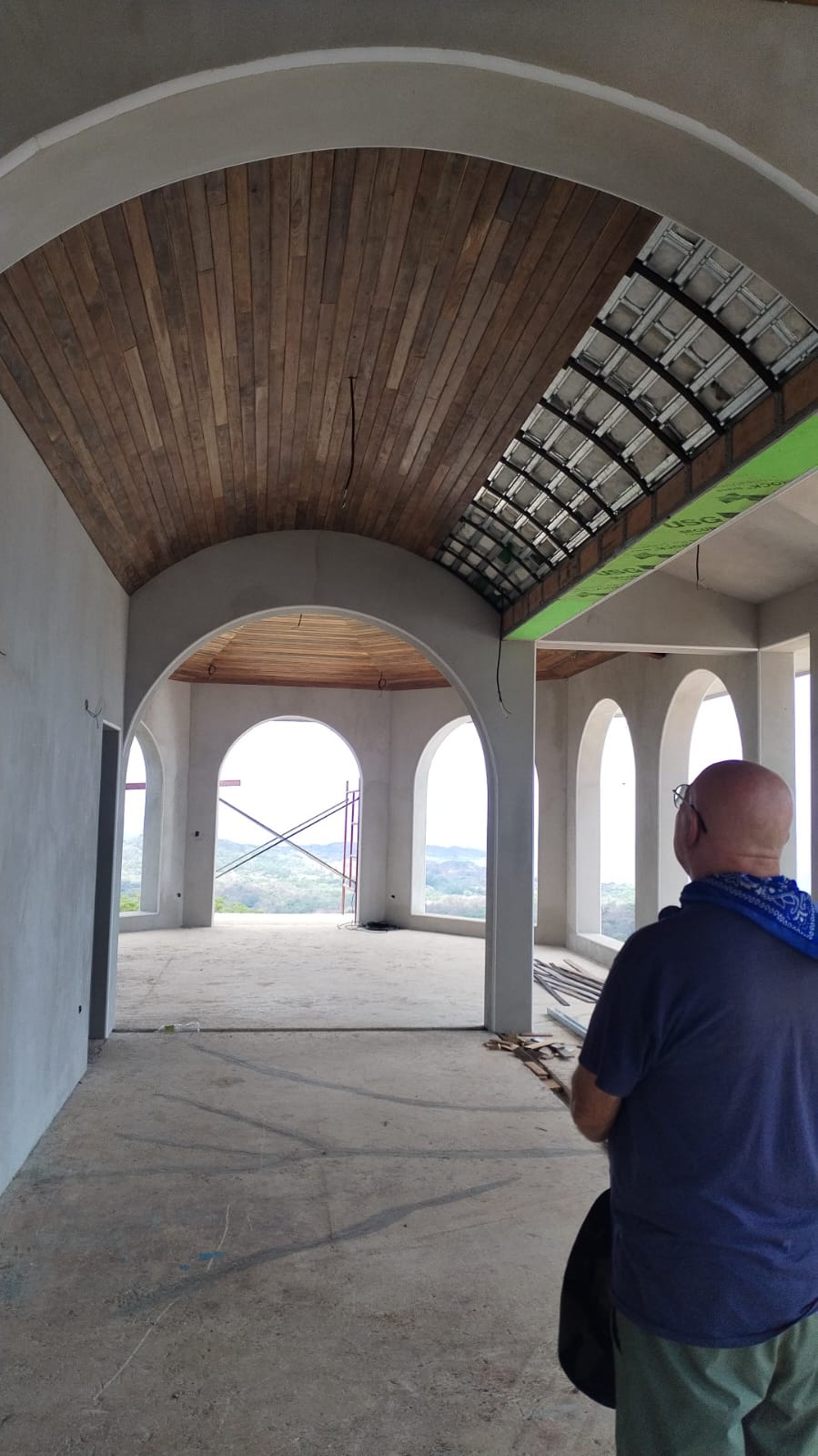 Un hombre observa una estructura en construcción con techos abovedados de madera y arcos abiertos.