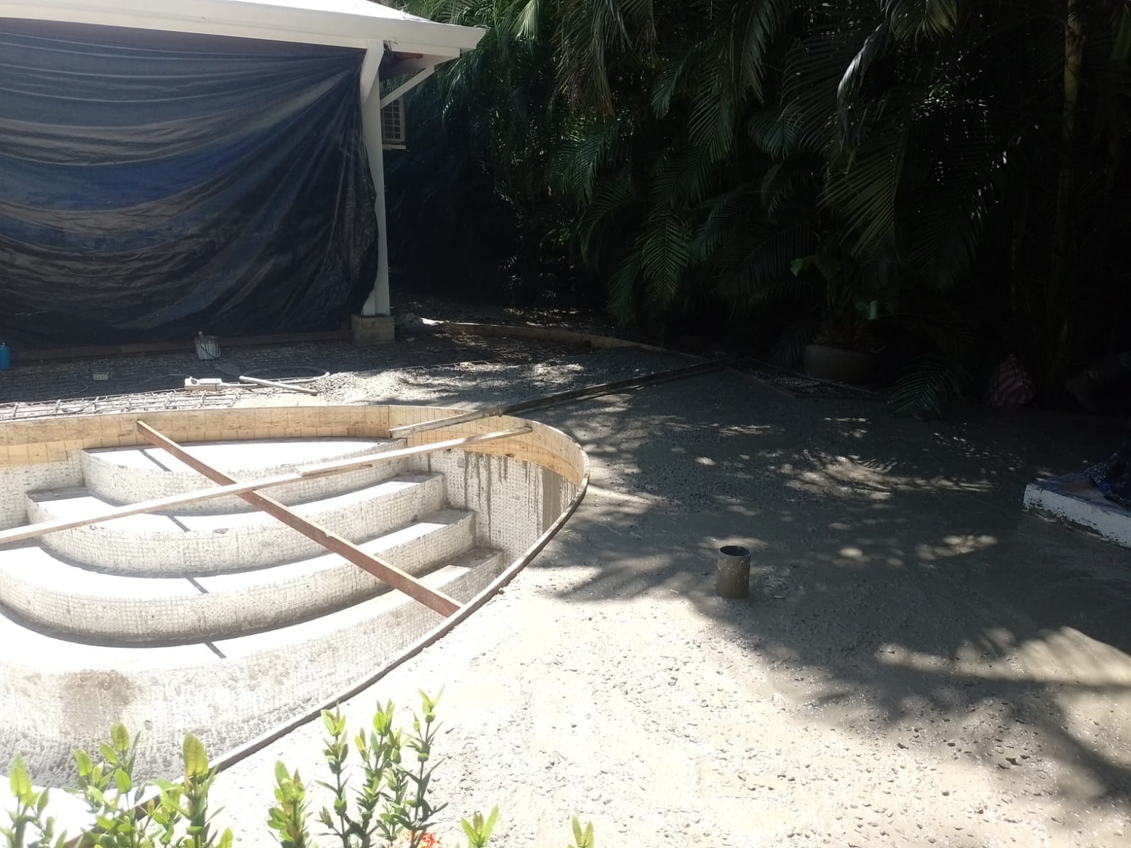 Se observa una piscina en proceso de construcción con escalones de mosaico y área de concreto fresco.
